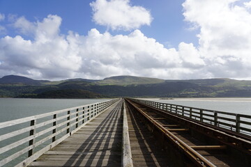 A railroad bridge over water with mountains in the background in Wales.
