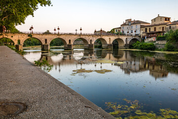 Fototapeta na wymiar Vue au coucher du soleil sur le Pont Tibère et sa réflexion sur les eaux du fleuve Vidourle à Sommières (Occitanie, France)