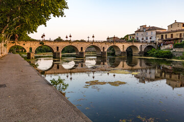 Vue au coucher du soleil sur le Pont Tibère et sa réflexion sur les eaux du fleuve Vidourle à...