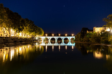 Fototapeta na wymiar Vue nocturne sur le Pont Tibère et sa réflexion sur les eaux du fleuve Vidourle à Sommières (Occitanie, France)