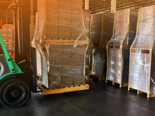 Worker driving forklift loading and unloading shipment carton boxes and goods on wooden pallet from container truck to warehouse cargo storage in logistics and transportation industrial 