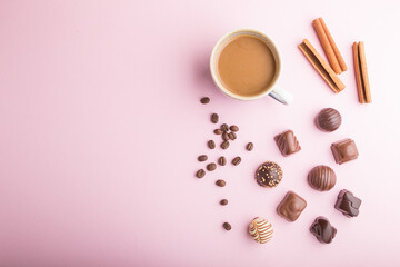 Different chocolate candies and a cup of coffee on a pink pastel background. top view, copy space.