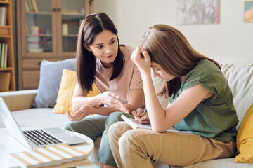 Young confident woman in casualwear helping her teenage daughter with homework