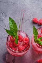 Fresh ice cold berry juice drink with mint, summer raspberry lemonade in two glass with straws on stone concrete background, angle view