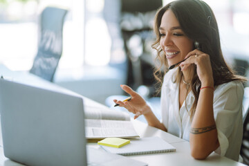 Young woman student wear wireless headphone study online. She learn language listen lecture watch webinar write notes look at laptop, distant education. Video call self-isolation during ncov situation