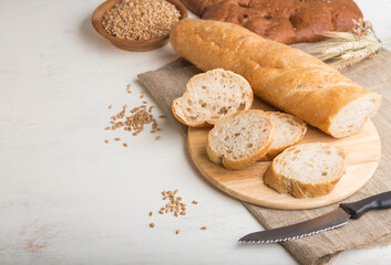 Sliced bread with different kinds of fresh baked bread on a white wooden background. side view, copy space.