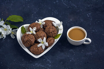 Still life with apple tree flowers and homemade chocolate cookies. Dessert for served for coffee break on a heart shaped plate. Snack on a spring day in the garden.