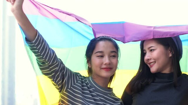 Happy loving homosexual lesbian LGBT couple with rainbow flag at city streets at sunset. Portrait of happy lesbian LGBT woman wraped herself in rainbow flag. slow motion