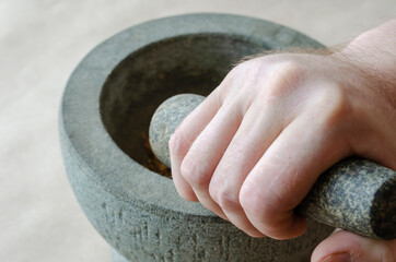 Hand grinds the dried roots of medicinal herbs in stone mortar.