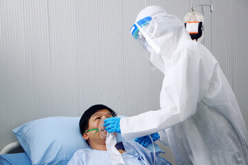 Medical doctor in Personal Protective Equipment or PPE clothing and use a respirator for Thai old man patient infected with the Covid 19 virus and treatment at hospital in Thailand