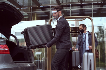 Hotel employee loading customer luggage into a car trunk