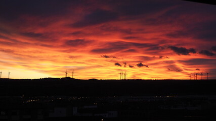 Paisaje en el que se ven los colores anaranjados del atardecer con molinos de un parque eólico al fondo.