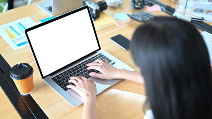 A woman is using a white blank screen computer laptop at the cluttered working desk.