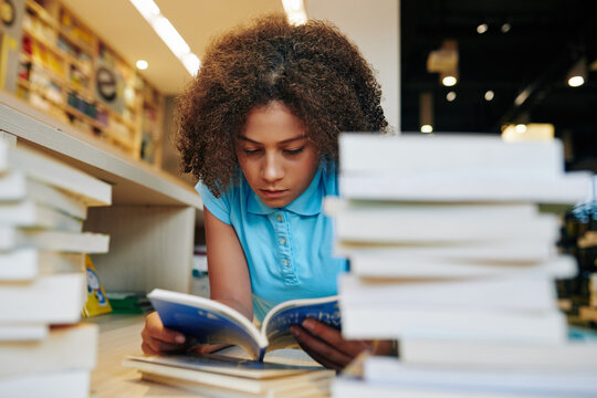 Seious teenage girl reading students book in library for big school project