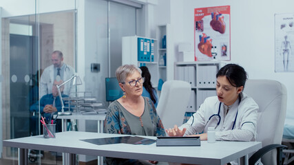 Obraz premium Doctor filling out prescription on digital tablet while consulting elderly senior retired woman. Healthcare in modern hospital or private clinic, disease prevention and consultation in medic office