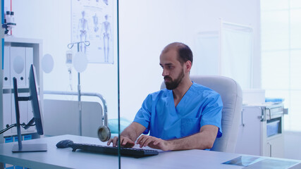 Assistant in blue medical uniform giving doctor patient x-ray image in hospital cabinet. Medic examining patient radiography before giving a treatment to cure his affection.