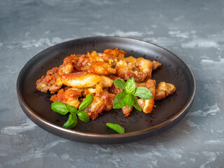 Lunch with chicken fillet on a ceramic dark plate and basil leaves on a gray background