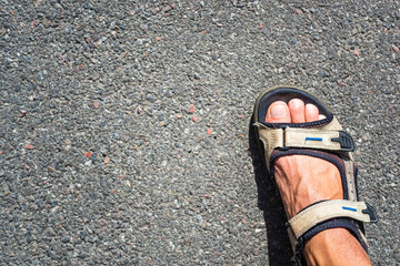 Tanned male legs in hiking sandals on the asphalt on a sunny day.