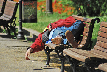 A homeless person takes a nap on a bench at the park