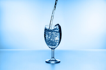 Pouring water into glass on blue background