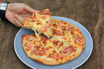 Young man hand holding a slice of Pizza in the bowl on wooden background with copy space