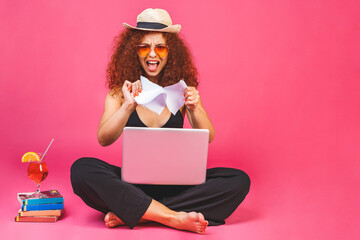 Summer business concept. Portrait of angry woman sitting on floor in lotus pose and holding laptop and cocktail isolated over pink background.