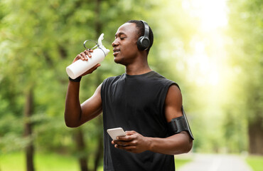African jogger drinking water and using smartphone