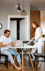 handsome guy work from home using laptop, smiling woman always near him, redhead lady and bearded guy are busy with their own business, woman sorting through the dishes