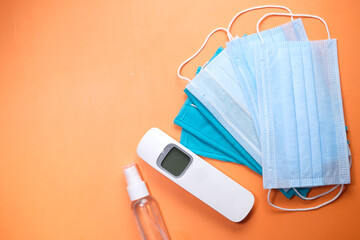 Surgical masks, thermometer and hand sanitizer on orange background 