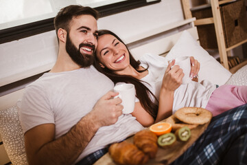 Obraz premium Young happy couple drinking coffee in bed at morning