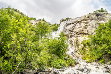 Waterfall on summer day in nature. Rapid water stream falling from rocks against blue sky on sunny summer day in countryside