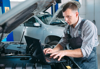 car mechanic using a computer laptop to diagnosing and checking up on car engines parts for fixing...