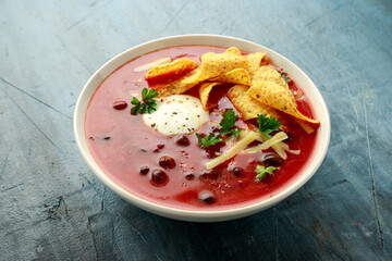 Mexican Chilli bean soup with yogurt, cheese, lime and tortilla chips in white bowl