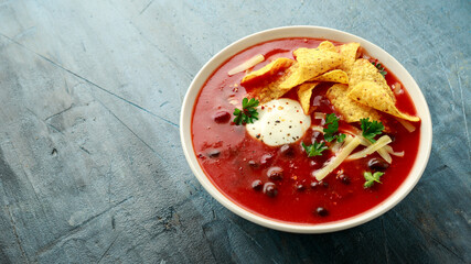 Mexican Chilli bean soup with yogurt, cheese, lime and tortilla chips in white bowl