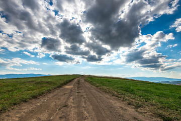 Dirt road leading to the top of the hill at summertime, vibrant white clouds on the blue sky.