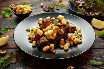 Roasted Pork chops with caramelized apples, walnuts and sage in black plate on wooden table
