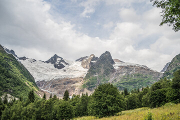 Beautiful mountain landscape in wooded area in summertime. Mighty mountains with snow and green array in cloudy weather.