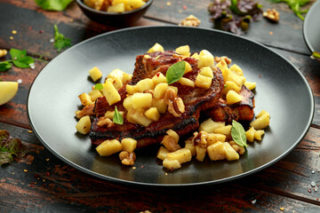 Roasted Pork chops with caramelized apples, walnuts and sage in black plate on wooden table