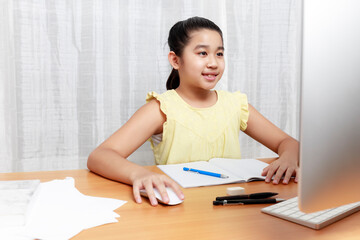 Naklejka premium Asian young little girl using pencil to do homework by herself. Student kid writing homework book. Girl use computer to study at home. Education homeschool concept.