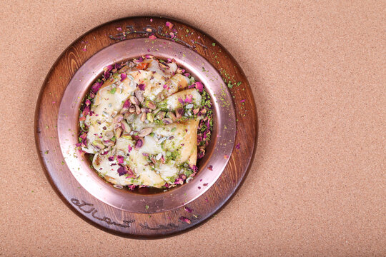 closeup of Turkish sugar dough sweet With pink pistachios top view on the wooden plate & white honey