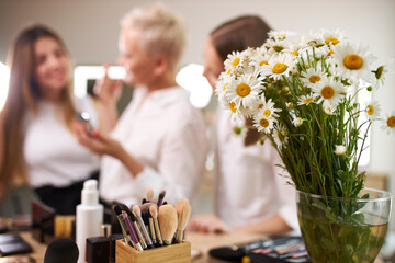close-up photo of beautiful flowers in a vase, make-up artists in the background, discussing