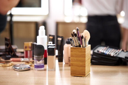 close-up photo of big amount of decorative cosmetics on table in beauty salon, wide variety of brushes, concealers, powders and other things