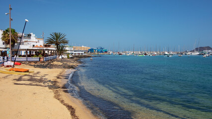Obraz premium Shallow beach near the promenade, lined up with restaurants and entertainment venues with ample views towards the yachts and vessels, Corralejo, Fuerteventura, Canary Islands, Spain