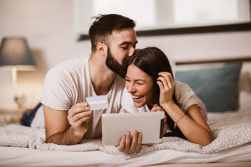 Young couple shopping online from the comfort of bedroom and using digital tablet and credit card