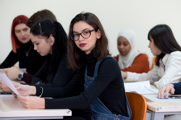 Exams Preparation. Group Of Multi-Ethnic Students Studying Together inside classroom while helping each other. Female student smiling into camera.