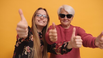 Young woman and trendy granny with sunglasses holding thumbs up. Studio shot. High quality photo