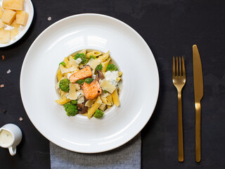 Pasta penne with salmon, broccoli, and pesto sauce on the black background. Flat lay.