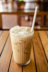Glass of iced coffee with paper straw on wooden table.
