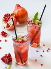 Pomegranate juice on a white background in glass glasses with iron straws.