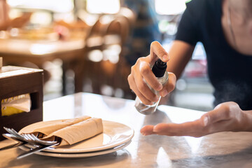 Close-up A woman's hand is using a hand sanitizer spray before eating in a restaurant. To kill...